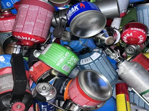 Ein Haufen verschiedener Gaskartuschen, darunter Primus und Optimus. Diese sind für Campingkocher gedacht, aber einige sehen aus, als wären sie für den Flugzeugtransport vorbereitet.