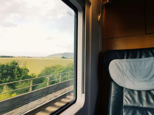 Blick aus dem Zugfenster auf grüne Felder und Hügel. Bequemer Sitzplatz im Abteil, bereit für die Reise durch den Euro city.
