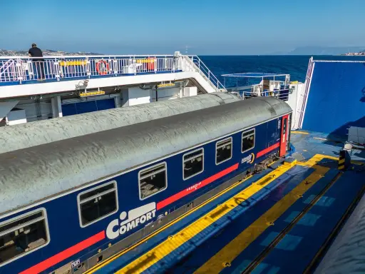 Ein blauer Nachtzug nach Palermo steht auf einer Fähre. Ein Mann blickt aufs Meer.