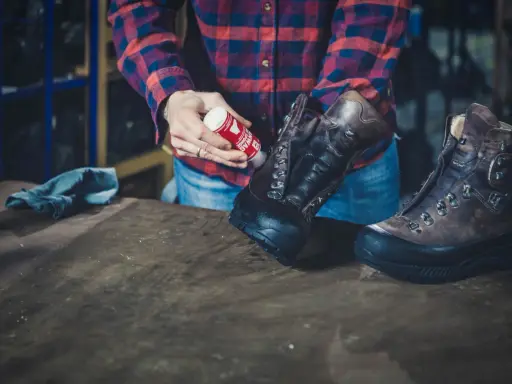 Mann pflegt Hanwag Schuhe mit einem roten Pflegeprodukt. Ein blaues Tuch liegt daneben.