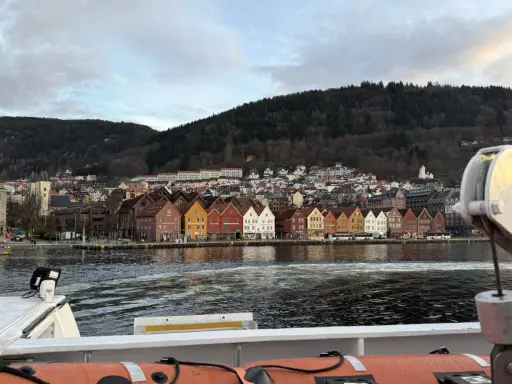 Bunte Holzhäuser am Kai von Bergen, mit einem bewaldeten Hügel im Hintergrund. Die bergen bahn ist hier nicht zu sehen, aber die Aussicht ist malerisch.