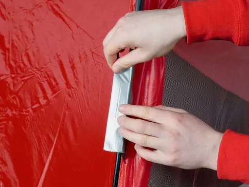 Hände reparieren ein rotes Zelt mit Klebeband.