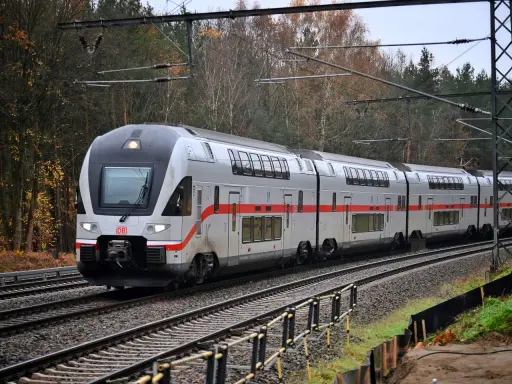 Ein moderner Doppelstockzug der Deutschen Bahn fährt durch eine herbstliche Landschaft. Die roten Streifen am Zug heben sich vom silbernen Lack ab.