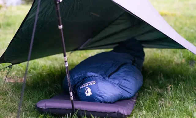Ein dunkelblauer Kunstfaser-Schlafsack liegt auf einer Isomatte unter einem Tarp. Perfekt für Outdoor-Abenteuer, auch wenn man ihn mal waschen muss.