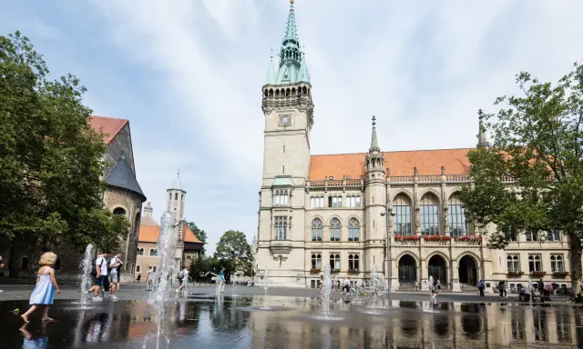 Kinder planschen im Brunnen vor dem Rathaus. Hier kann man in Braunschweig viel erleben, z.B. den Dom besichtigen.