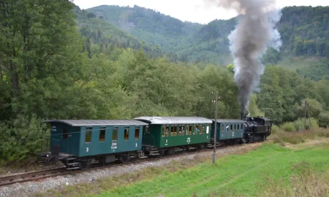 Dampflok der slowakischen Bahn fährt durch eine grüne Landschaft.