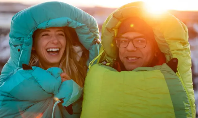 Glückliches Paar in Schlafsäcken bei Sonnenuntergang. Die Frage welcher Schlafsack bei welcher Temperatur ist hier wohl gelöst!
