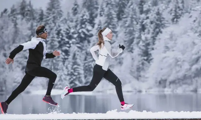 Zwei Läufer in warmer Winterkleidung genießen einen Lauf im Schnee.