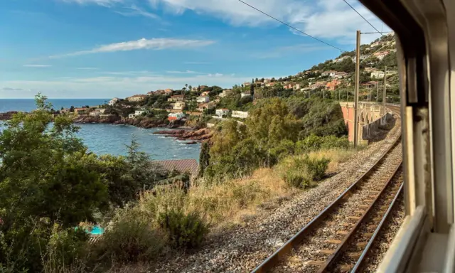 Blick aus dem Fenster eines Nachtzugs Paris Nizza auf eine Küstenlandschaft mit Häusern, Meer und Bahngleisen.