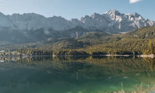 Spiegelglatter See vor bewaldeten Bergen. Ein Ort, der zum Camping am Staffelsee einlädt.