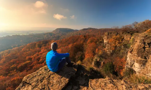 Ein Wanderer genießt den Ausblick auf die herbstliche Landschaft Norddeutschlands von einem Felsvorsprung.