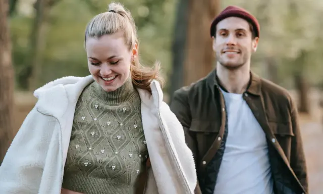 Ein lächelndes Paar im Freien. Sie trägt einen Strickpullover und eine Lammfelljacke, er eine Jacke und Mütze. Perfekt, um was anziehen bei 15 Grad.
