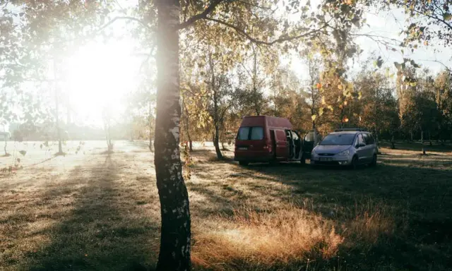 Sonnenaufgang im Herbst. Ein roter Camper und ein silberner Van stehen auf einer Wiese. Das ist Freiheit, das ist was ist wildcampen.