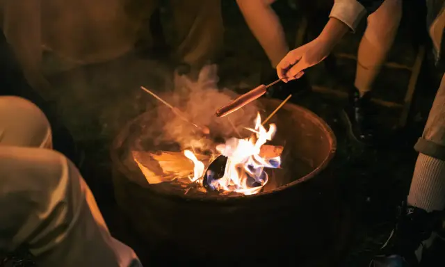 Kinder machen Feuer und rösten Würstchen über der Flamme.