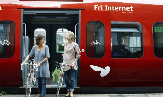 Zwei Frauen mit Fahrrädern steigen in einen roten **denmark train** nach Kopenhagen.