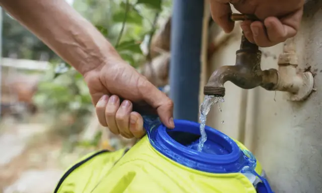 Wasser fließt aus einem alten Wasserhahn in eine gelbe Trinkblase. Nach dem Befüllen muss die Trinkblase trocknen.