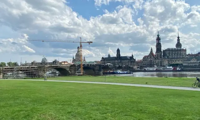 Grüne Wiese mit Blick auf die Elbe, die Brücke und die Frauenkirche. Ein Radfahrer genießt die Aussicht, um Dresden zu erleben.