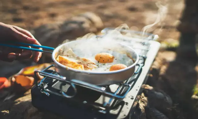 Spiegeleier und Brot brutzeln in einer Pfanne auf einem Gaskocher. Perfekte Camping Rezepte für unterwegs.