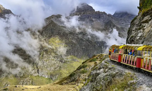 Gelber Zug fährt durch neblige Berglandschaft in den Pyrenäen, Frankreich.