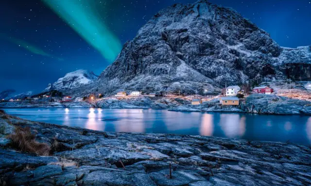 Ein malerisches Dorf in Norwegen im Winter, beleuchtet von den Nordlichtern und dem Sternenhimmel.