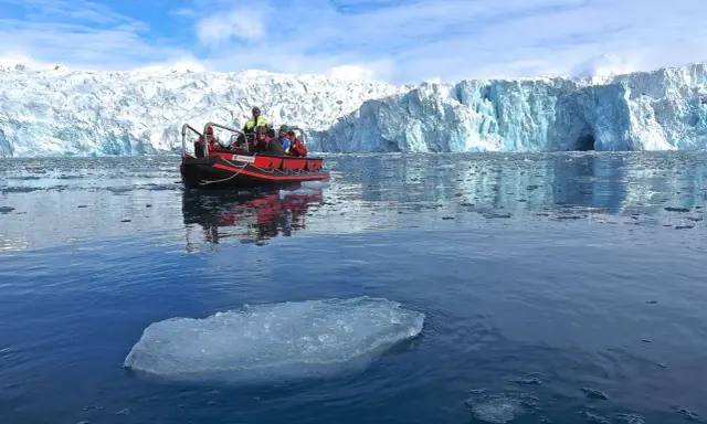Ein Schlauchboot mit Touristen fährt auf dem eisigen Meer vor einem riesigen Gletscher. Ein wahrer "ice express" in die Arktis.