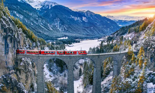 Roter Zug überquert eine Steinbrücke in verschneiter Schweizer Alpenlandschaft. Ein perfektes reiseziel schweiz.