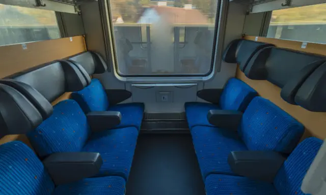 Leere Sitze im Nachtzug nach Stockholm. Blaue Polster mit orangefarbenen Punkten und schwarze Armlehnen laden zur Reise ein.