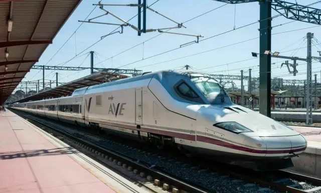 Moderner, weißer Renfe ave zug mit lila Akzenten steht auf Gleisen unter einem Bahnhofsdach.