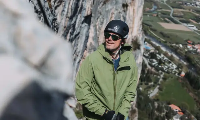 Bergsteiger in grüner, wasserdichter Jacke und Helm blickt in die Ferne. Die Ausrüstung zeigt, was wasserdicht bedeutet: Schutz bei jedem Wetter.