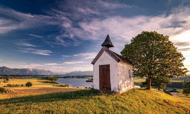 Kleine Kapelle auf einem Hügel mit Blick auf einen See und Berge. Ein **Geheimtipp Urlaub November Deutschland** für ruhige Tage.