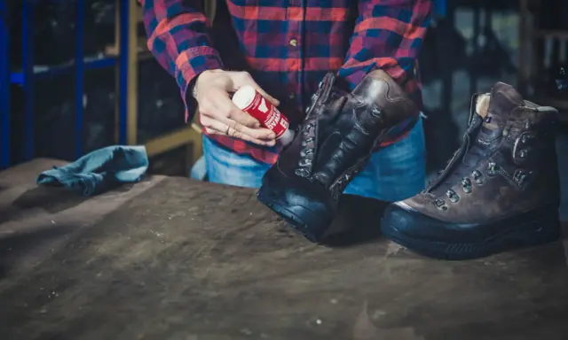 Mann pflegt Hanwag Schuhe mit einem roten Pflegeprodukt. Ein blaues Tuch liegt daneben.