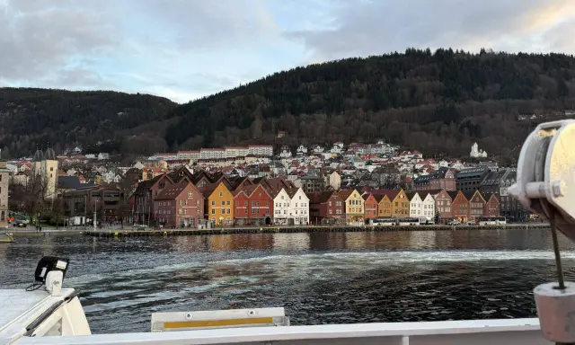 Bunte Holzhäuser am Kai von Bergen, mit einem bewaldeten Hügel im Hintergrund. Die bergen bahn ist hier nicht zu sehen, aber die Aussicht ist malerisch.