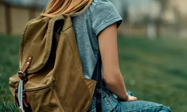 Mädchen mit braunem Rucksack sitzt im Gras. Der Rucksack ist bereit für das Waschen, um ihn wieder frisch zu machen.