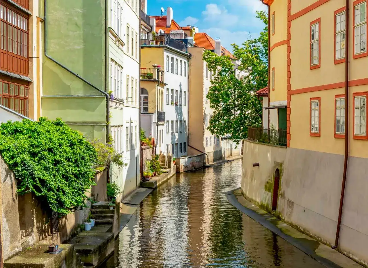 Malerischer Kanal in Prag, ein idyllisches Motiv f&uuml;r Ausflugsziele. Bunte H&auml;user s&auml;umen das Wasser, &uuml;ppiges Gr&uuml;n rankt sich an den Mauern empor.
