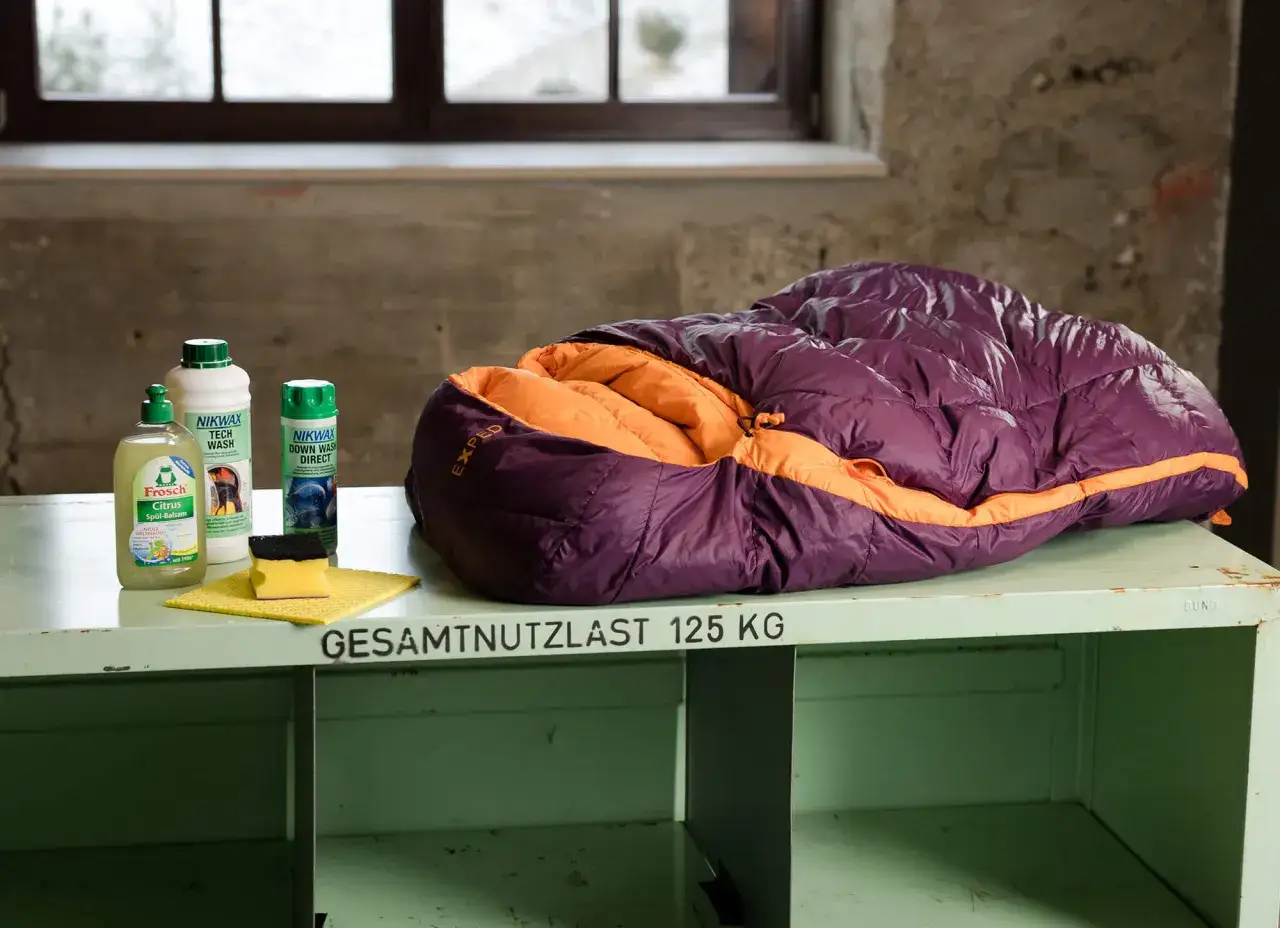 Lila-orangefarbener Exped-Schlafsack bereit zum Schlafsack waschen, daneben Reinigungsmittel und Schwamm.