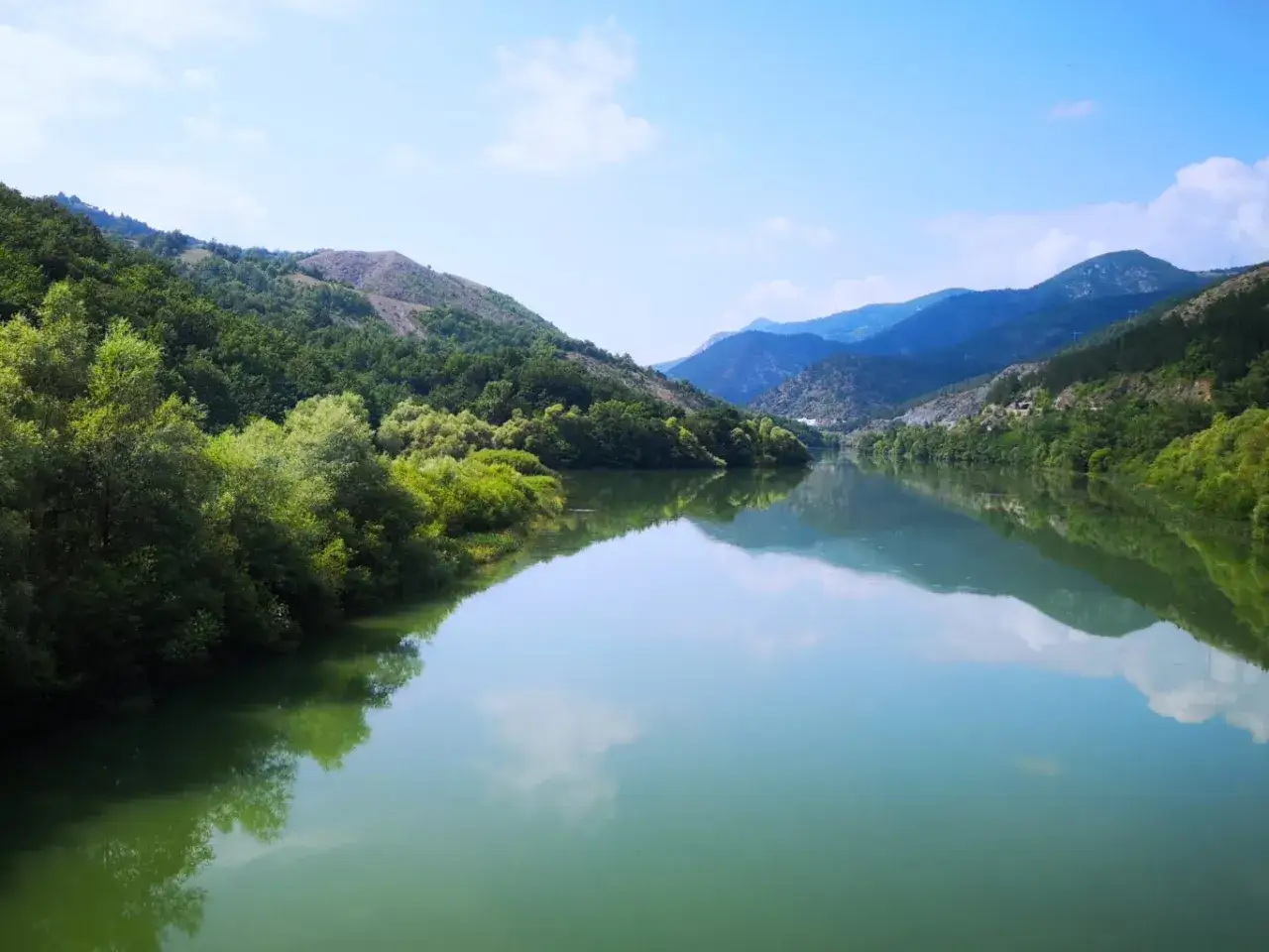 Gr&uuml;ne Berge spiegeln sich in einem ruhigen Fluss in Montenegro. Ein Zug f&auml;hrt durch diese malerische Landschaft.