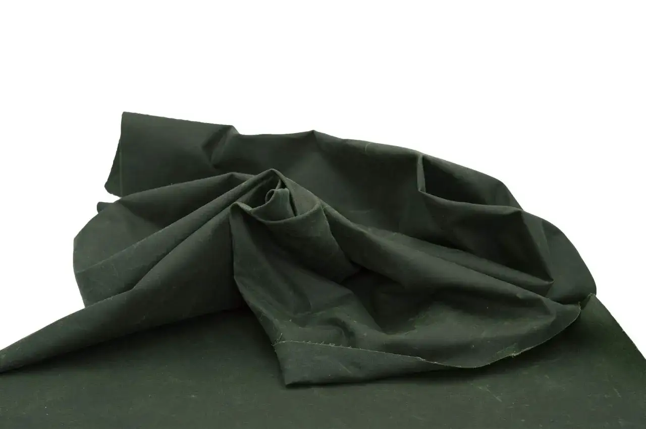 Dunkelgrüner Stoff, der sich zu einer Rolle formt. Ideal für Outdoor-Bekleidung, z.B. eine Jacke im Stil g 1000.