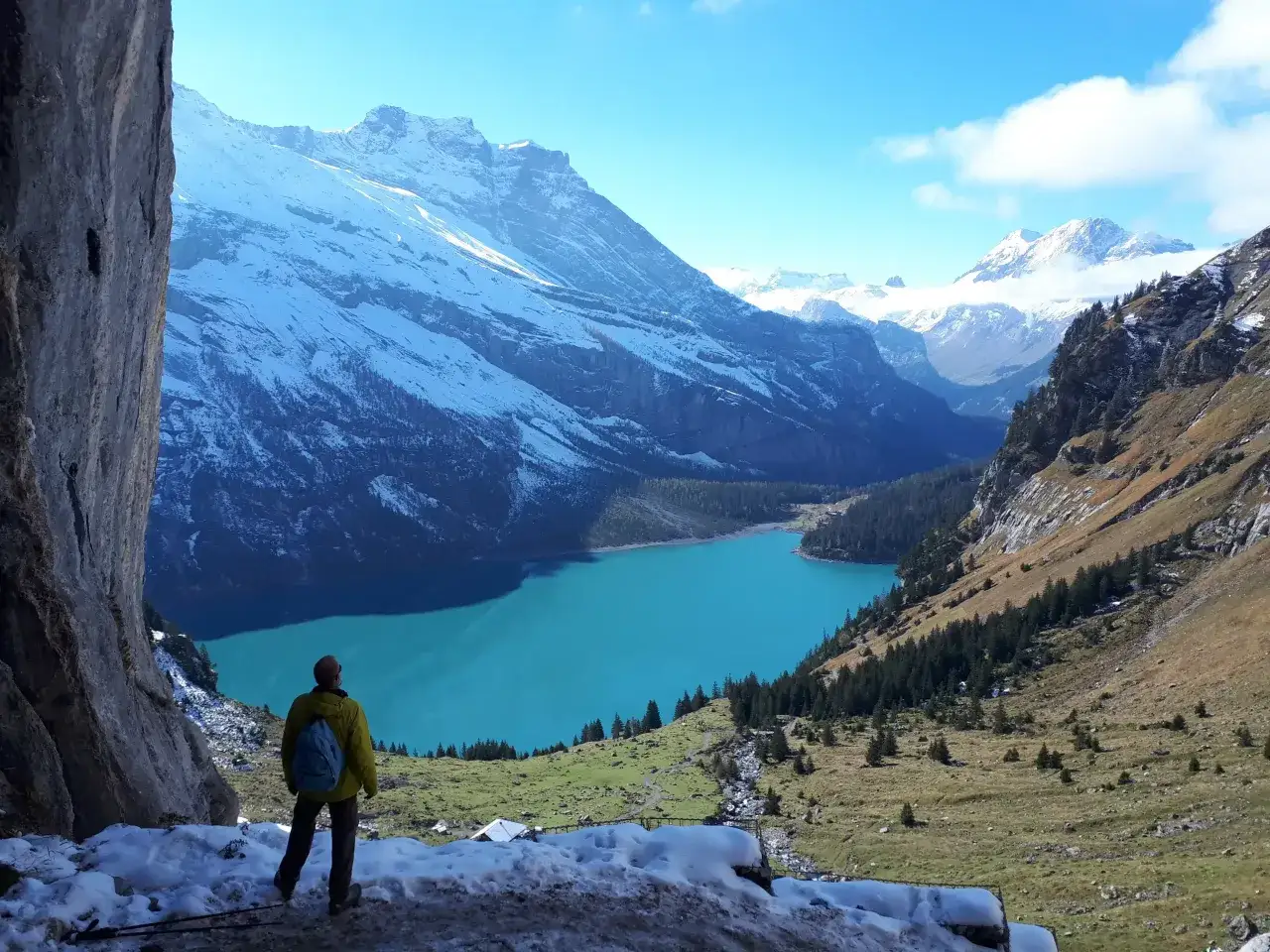 Ein Wanderer blickt auf einen t&uuml;rkisfarbenen See vor schneebedeckten Bergen. Ein perfektes reiseziel schweiz f&uuml;r Naturliebhaber.