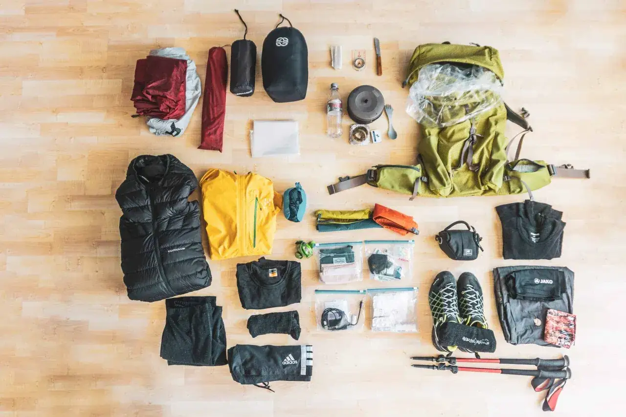 Die Packliste für den Wanderurlaub umfasst Rucksack, Zelt, Schlafsack, Kleidung, Schuhe, Wanderstöcke und Kochutensilien.