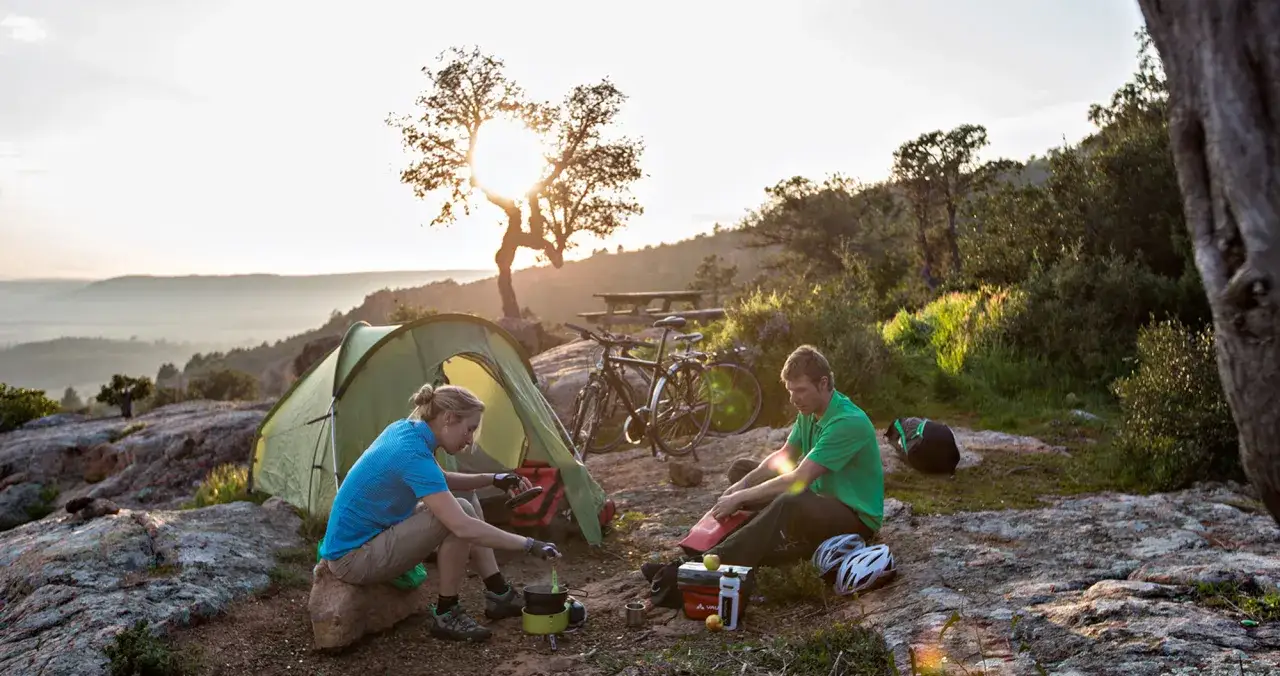 Ein Paar genießt das wildcampen Italien bei Sonnenuntergang. Fahrräder stehen neben dem Zelt, während sie kochen.