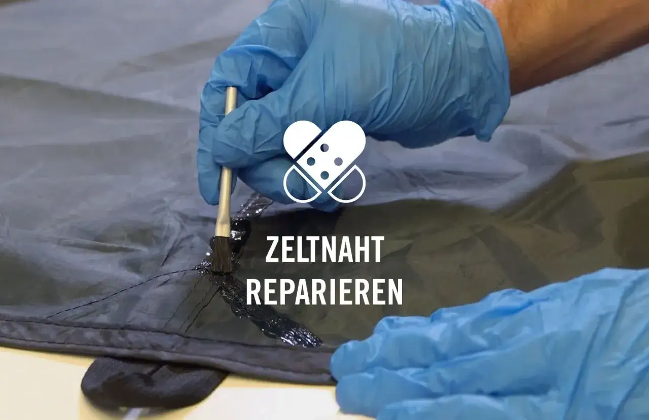 Mit blauen Handschuhen wird eine Naht am Zelt reparieren. Ein Pinsel trägt schwarze Dichtungsmasse auf die Naht auf.