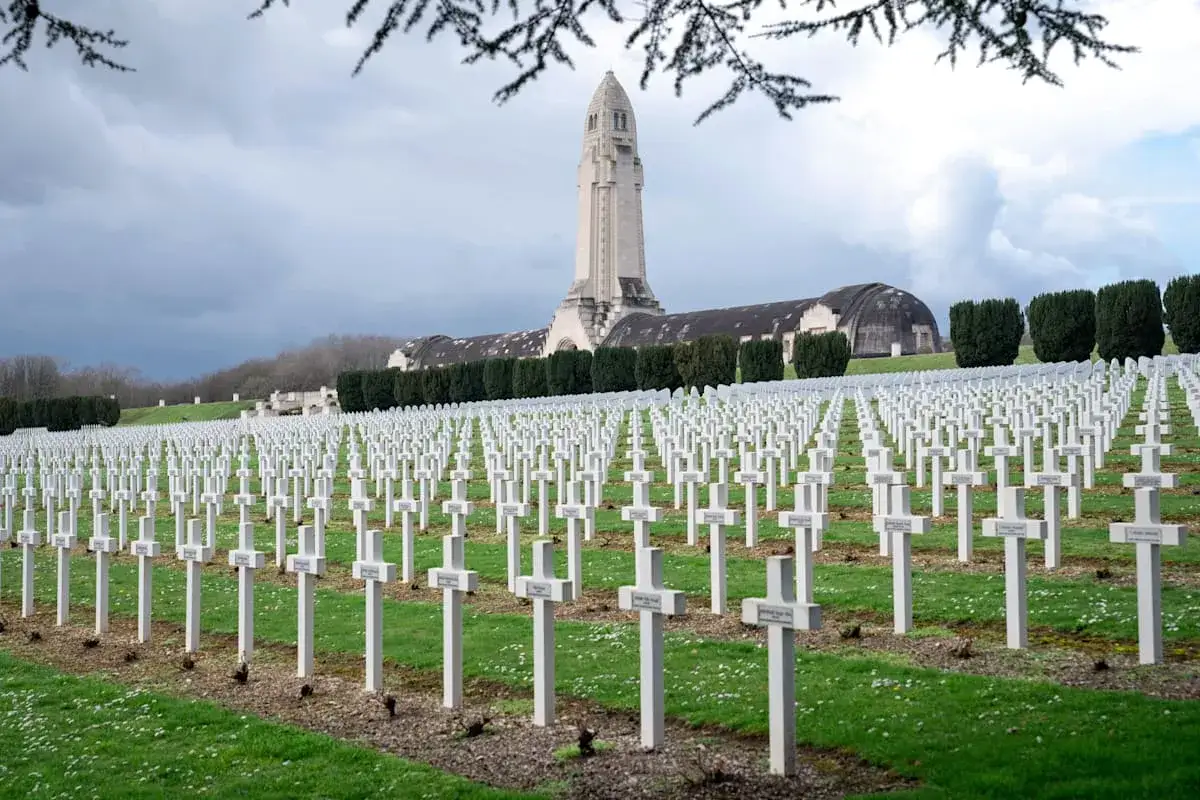 Reihen wei&szlig;er Kreuze auf einem Friedhof, ein Denkmal im Hintergrund. Ein Ort des Gedenkens und des dark tourism.