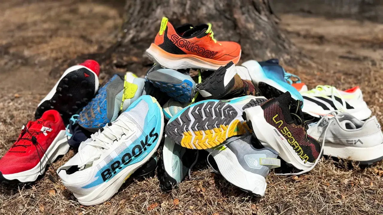 Bunte Trailrunningschuhe mit groben Sohlen liegen im Gras. Sie sind f&uuml;r unwegsames Gel&auml;nde konzipiert.