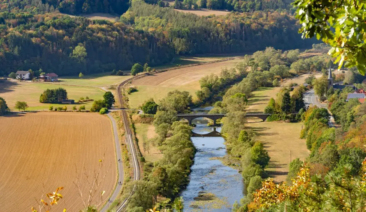 Idyllisches Tal in Hessen mit Fluss, Brücke, Bahngleisen und Feldern. Perfekt für einen erholsamen Urlaub.