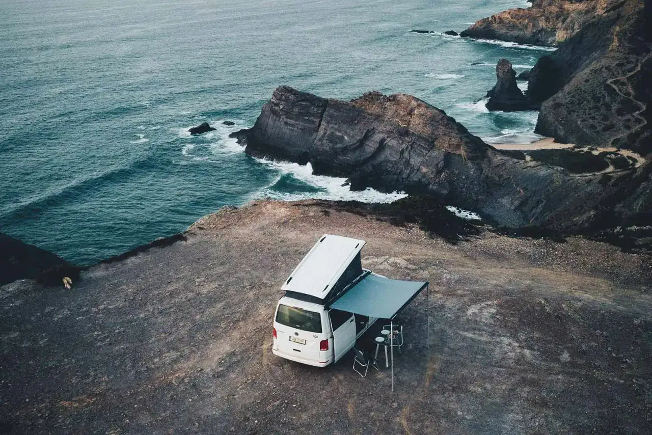 Ein Campervan mit ausgefahrenem Sonnensegel steht auf einer Klippe mit Blick auf das Meer. Perfekt f&uuml;r wildcampen Spanien.