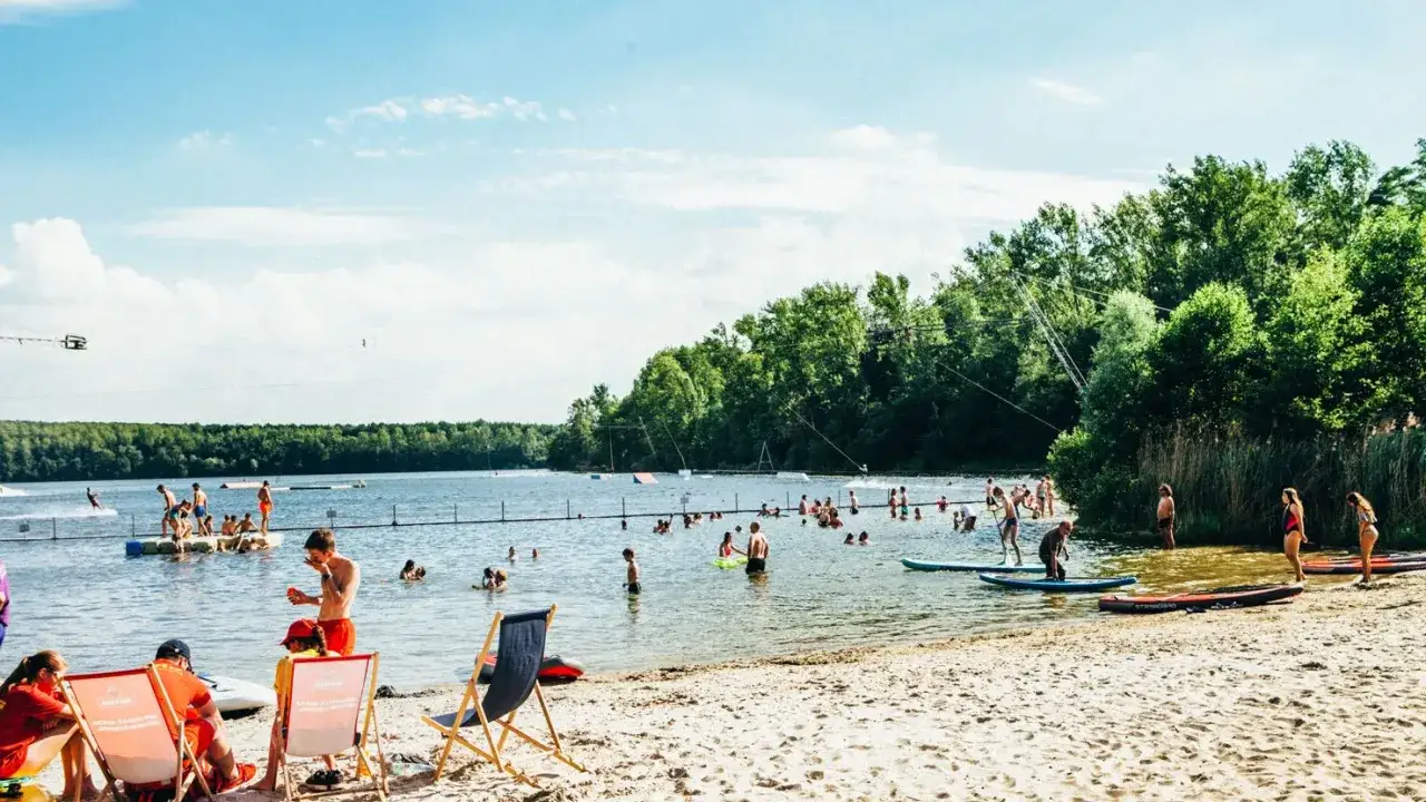 Sonniger Tag am See in NRW: Menschen planschen, paddeln und entspannen am Strand. FKK-Fans genie&szlig;en die Freiheit.