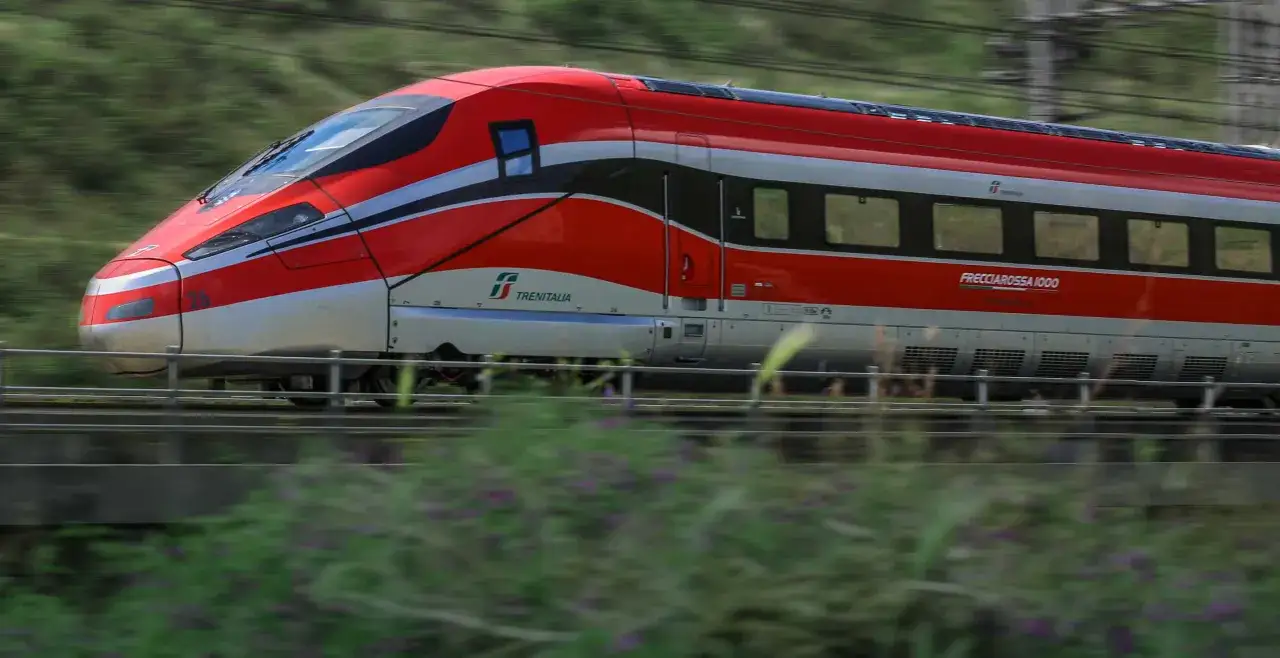 Ein roter italienischer Schnellzug, der Frecciarossa 1000, rast durch die Landschaft.