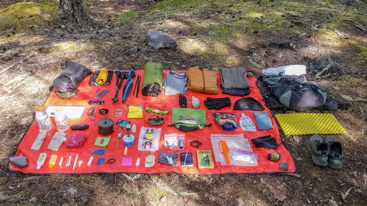 Wander-Essentials ausgebreitet: Rucksack, Kleidung, Kocher, Erste-Hilfe-Set, Schuhe und mehr für ein Abenteuer.