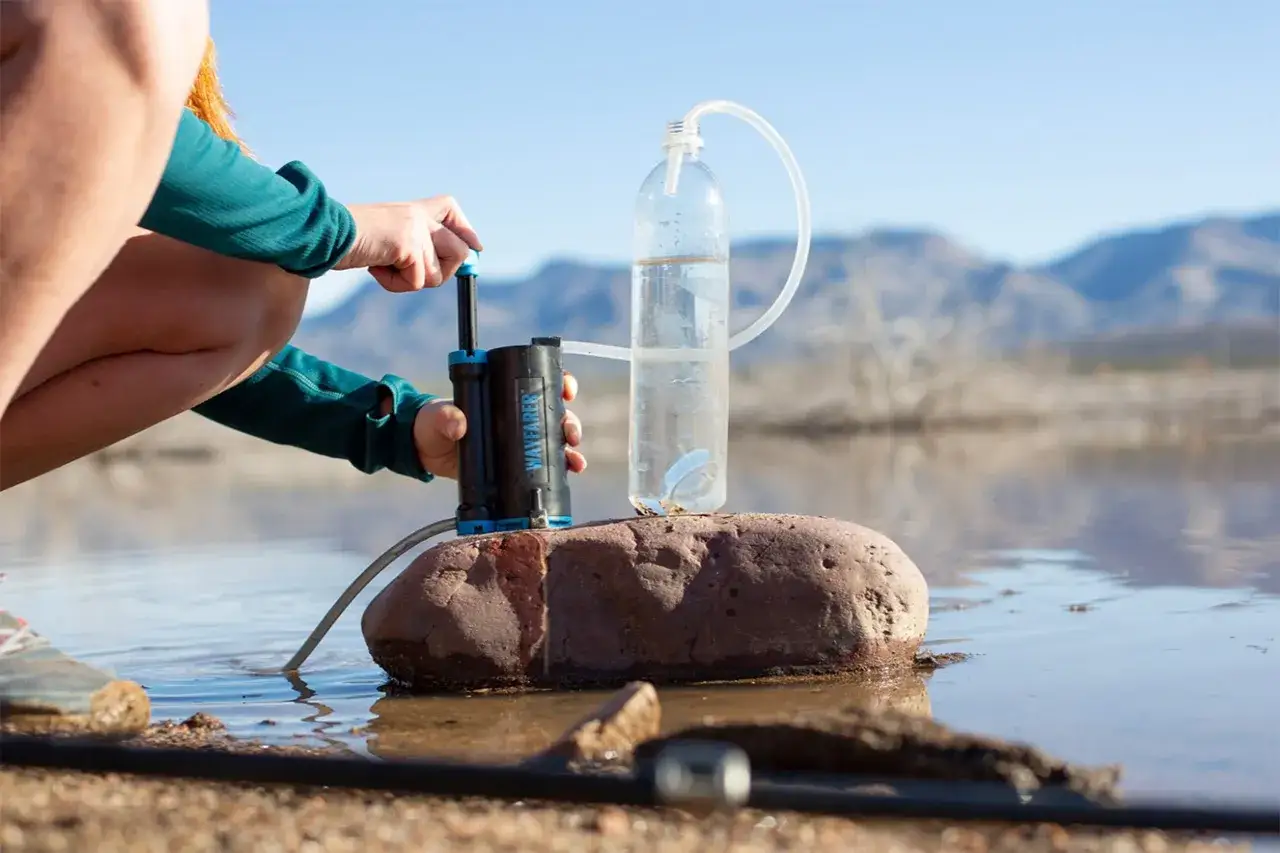 Outdoor-Wasserfilter-Test: Eine Person nutzt einen tragbaren Wasserfilter, um Wasser in eine Flasche zu pumpen.
