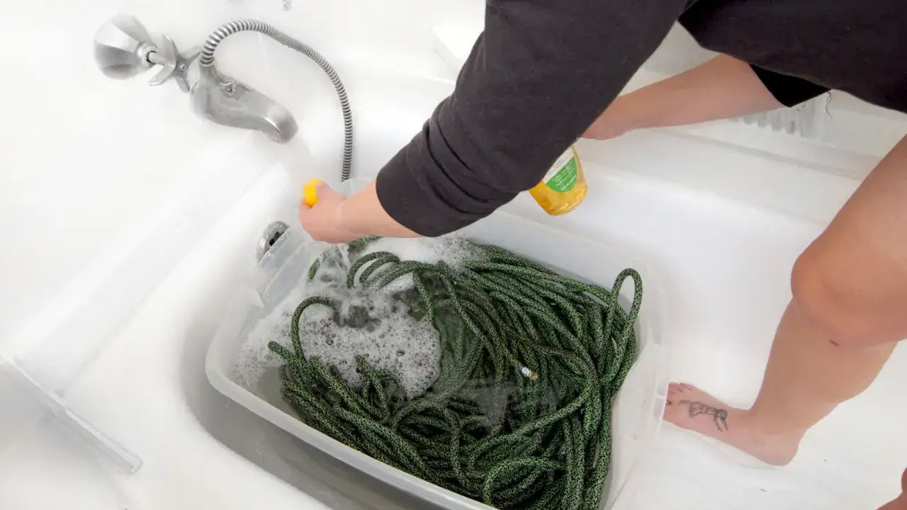 Person wäscht ein grünes Kletterseil in einer Wanne mit Seifenwasser.